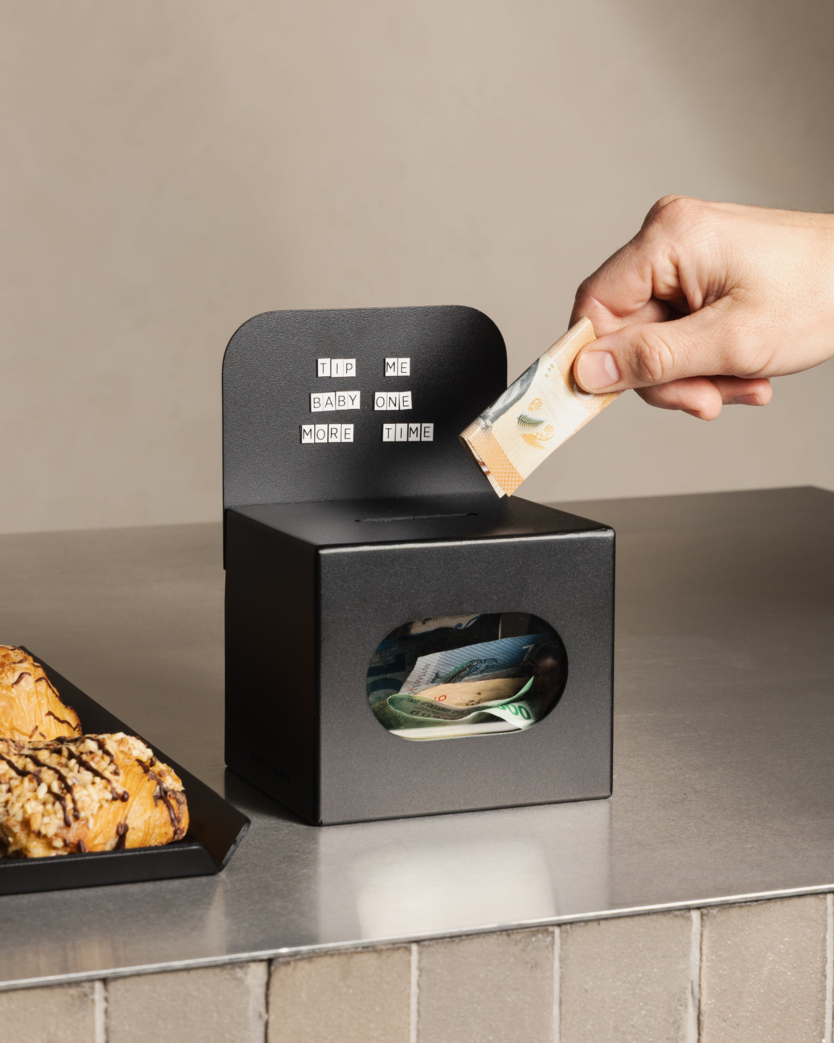 Customer placing a banknote into the black FOLD Tip Box on a café counter