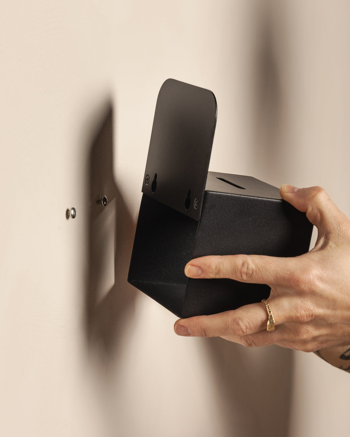 Mounting the black FOLD Tip Box onto wall screws using its keyhole fixings