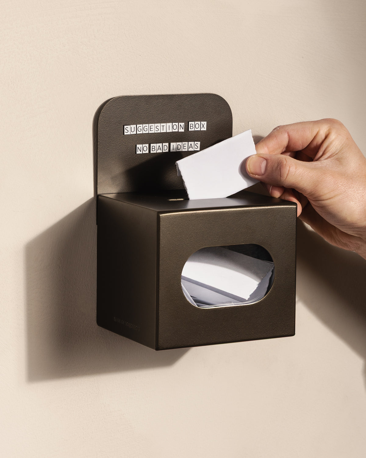 Customer posting a suggestion card into the wall-mounted bronze FOLD Tip Box
