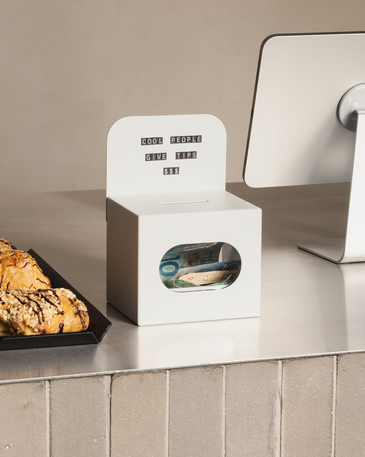 White FOLD Tip Box by Made of Tomorrow on a café counter beside pastries and a payment terminal